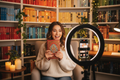 Excited young woman on BookTok holding up a hardcover book with cozy bookshelf background